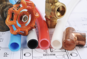 Different colored plastic tubing with other plumbing tools lying on top of a blue print.