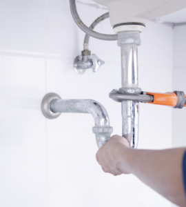 Technician's hand securing a silver under-sink pipe in a home's bathroom. White tile wall behind sink.